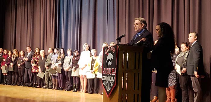 Jackson Board of Education President John Burnetsky (at podium) joins Board Vice President Sharon Dey in naming the 2019 Teachers of the Year and Educational Services Professional of the Year who are standing on the Jackson Memorial High School Fine Arts Auditorium stage. (Photo by Bob Vosseller)