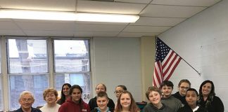 Dina Nagy’s sixth grade class poses beneath their new flag with Bob and Darlene Scheiderman and Superintendent Loren Fuhring. (Photo by Chris Lundy)